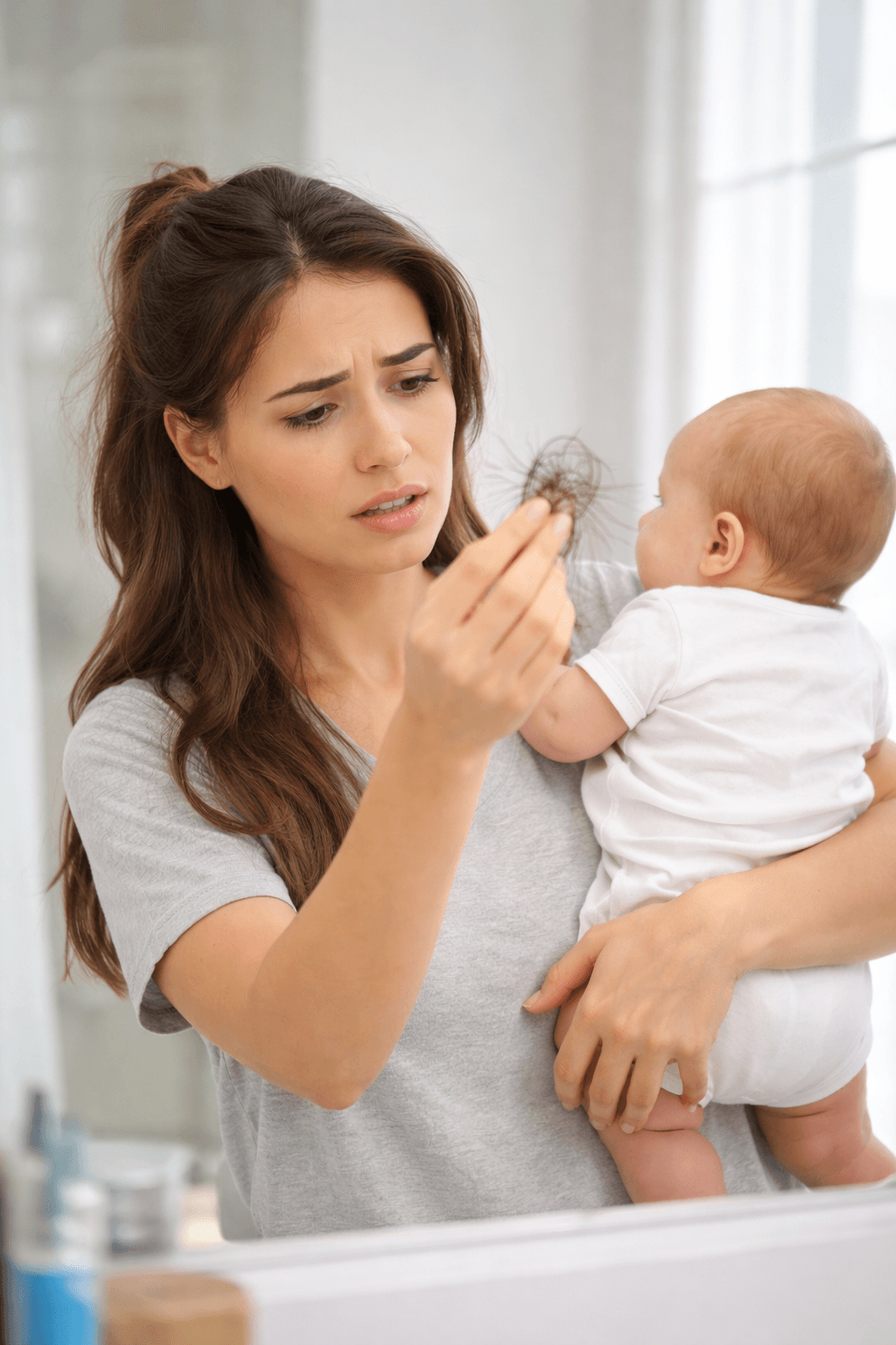 New mom holding her baby examines a small clump of shed hair—common postpartum shedding that often peaks 3–4 months after delivery. 